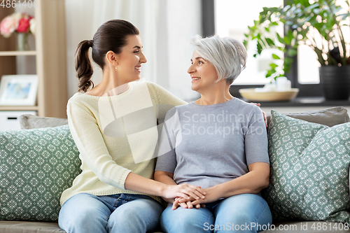 Image of senior mother with adult daughter hugging at home