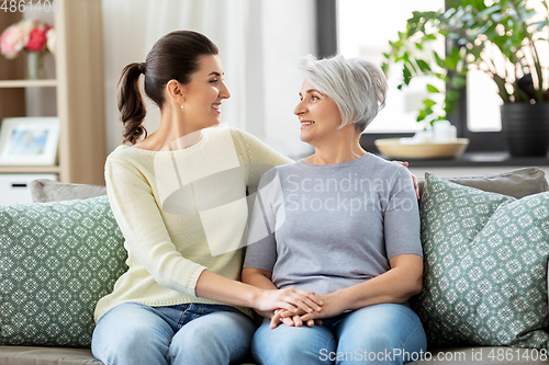 Image of senior mother with adult daughter hugging at home