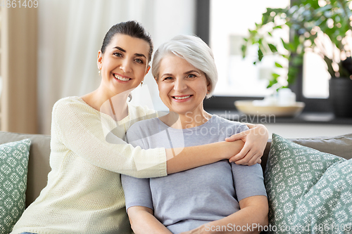 Image of senior mother with adult daughter hugging at home