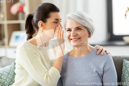 Image of adult daughter whispering secret to senior mother