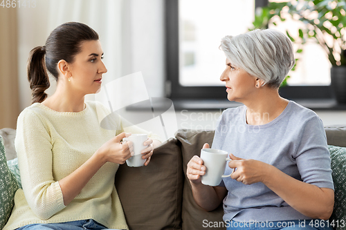 Image of senior mother and adult daughter drinking coffee