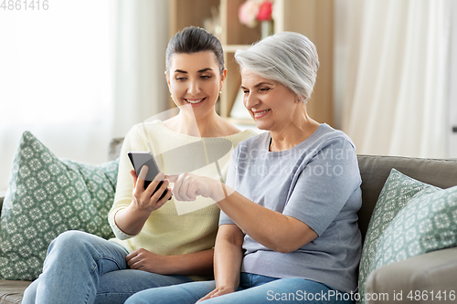 Image of daughter and senior mother with smartphone at home