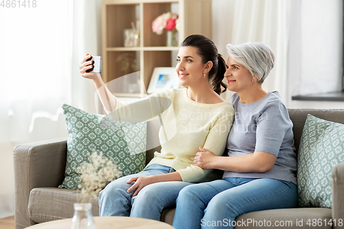 Image of senior mother with daughter taking selfie at home