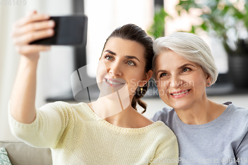 Image of senior mother with daughter taking selfie at home