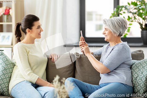 Image of senior mother photographing adult daughter at home