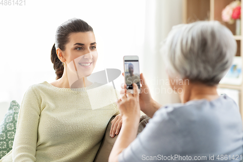 Image of senior mother photographing adult daughter at home