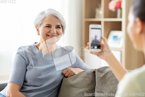 Image of adult daughter photographing senior mother at home