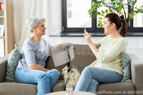 Image of adult daughter photographing senior mother at home