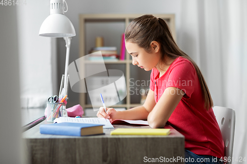 Image of student girl with book writing to notebook at home