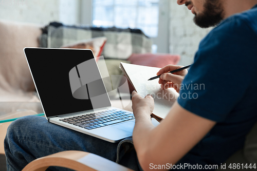 Image of Young focused man studying at home during online courses or free information by hisself