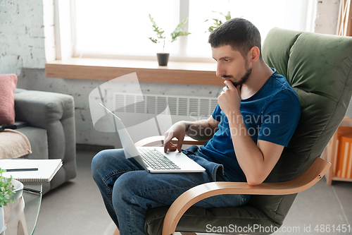 Image of Young focused man studying at home during online courses or free information by hisself