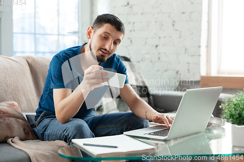 Image of Young focused man studying at home during online courses or free information by hisself