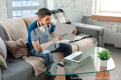 Image of Young focused man studying at home during online courses or free information by hisself