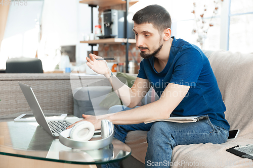 Image of Young focused man studying at home during online courses or free information by hisself