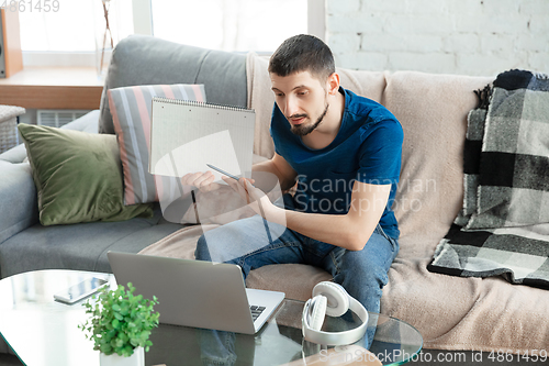 Image of Young focused man studying at home during online courses or free information by hisself