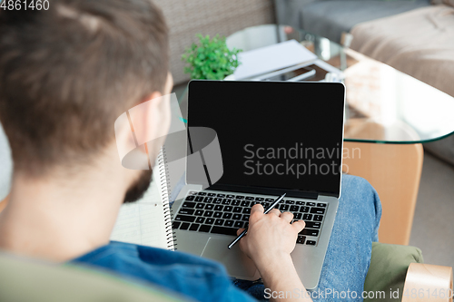 Image of Young focused man studying at home during online courses or free information by hisself