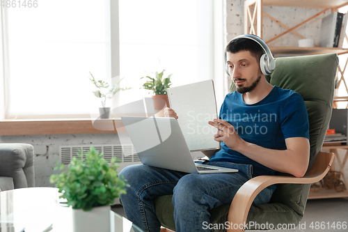 Image of Young focused man studying at home during online courses or free information by hisself