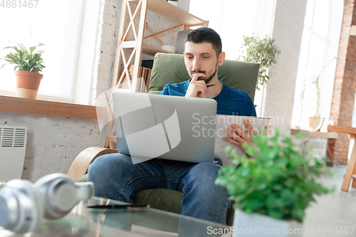 Image of Young focused man studying at home during online courses or free information by hisself