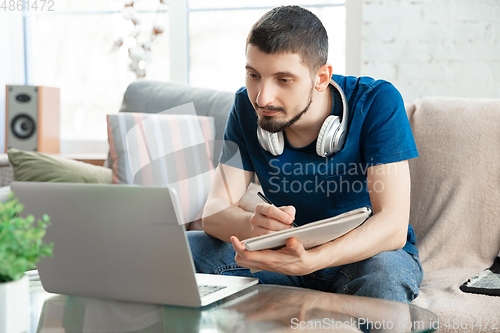 Image of Young focused man studying at home during online courses or free information by hisself