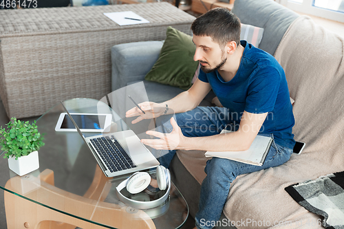 Image of Young focused man studying at home during online courses or free information by hisself