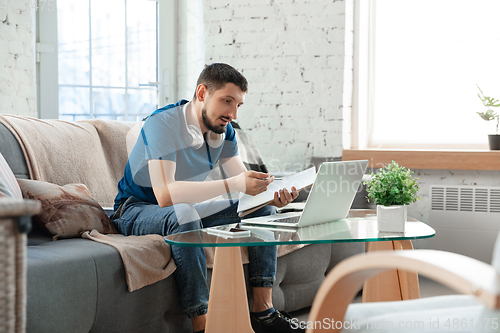 Image of Young focused man studying at home during online courses or free information by hisself