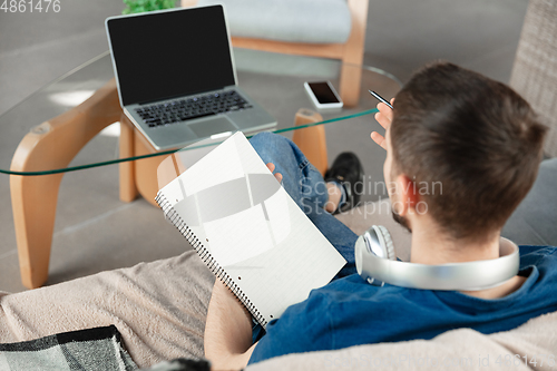 Image of Young focused man studying at home during online courses or free information by hisself