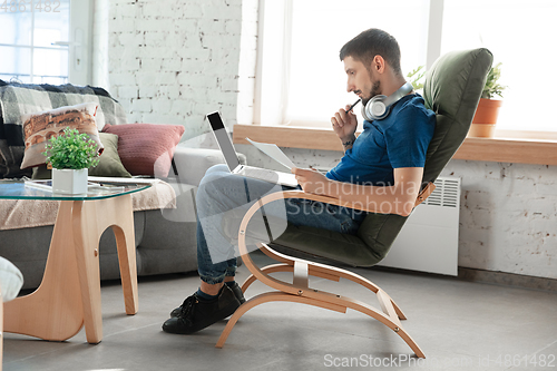 Image of Young focused man studying at home during online courses or free information by hisself