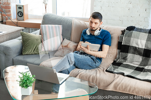 Image of Young focused man studying at home during online courses or free information by hisself