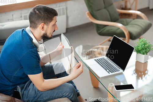 Image of Young focused man studying at home during online courses or free information by hisself