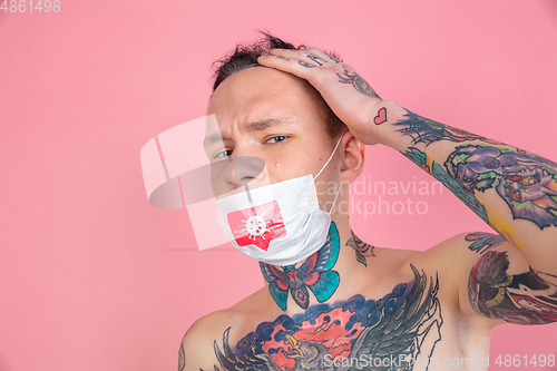 Image of Young man with freaky appearance on pink background wearing face mask with coronavirus model