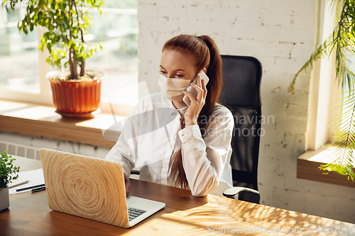 Image of Woman working in office alone during coronavirus or COVID-19 quarantine, wearing face mask