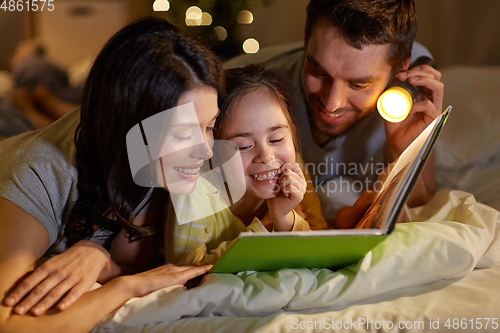 Image of happy family reading book in bed at night at home