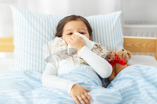 Image of sick girl lying in bed and blowing nose at home