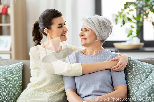 Image of senior mother with adult daughter hugging at home