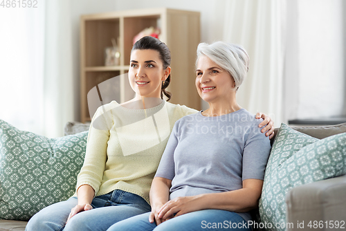 Image of senior mother with adult daughter hugging at home