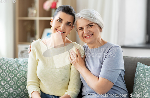 Image of senior mother with adult daughter hugging at home