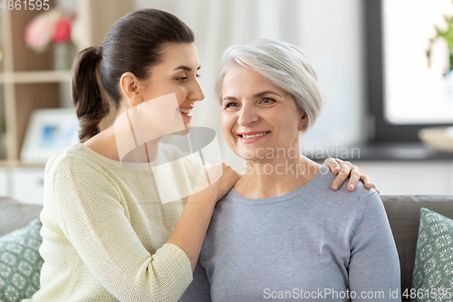 Image of senior mother with adult daughter hugging at home