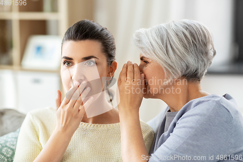 Image of senior mother whispering secret to adult daughter