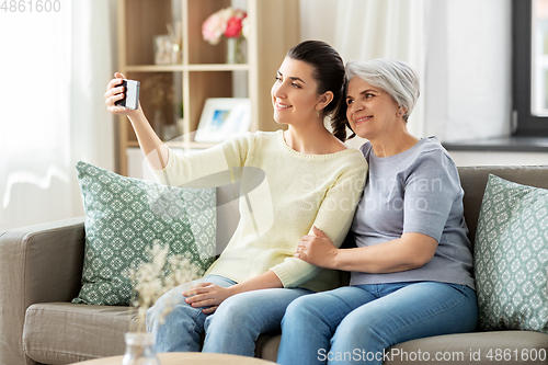 Image of senior mother with daughter taking selfie at home