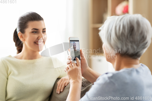 Image of senior mother photographing adult daughter at home