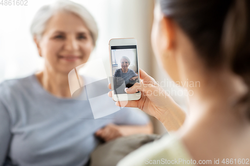 Image of adult daughter photographing senior mother at home