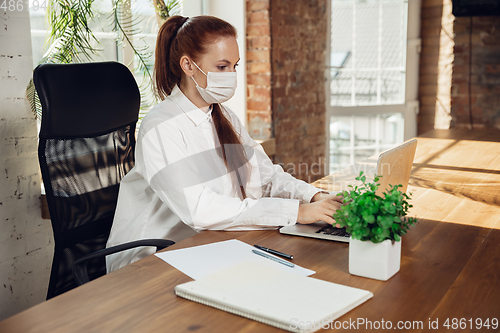 Image of Woman working in office alone during coronavirus or COVID-19 quarantine, wearing face mask