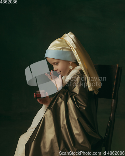 Image of Medieval little girl as a lady with a pearl earring on dark studio background. Concept of comparison of eras, childhood. Stylish creative design, art vision, new look of artwork.