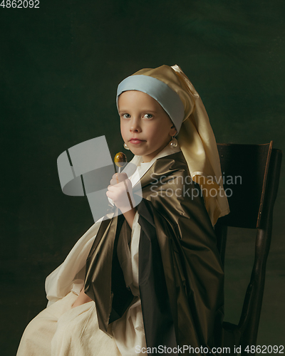 Image of Medieval little girl as a lady with a pearl earring on dark studio background. Concept of comparison of eras, childhood. Stylish creative design, art vision, new look of artwork.