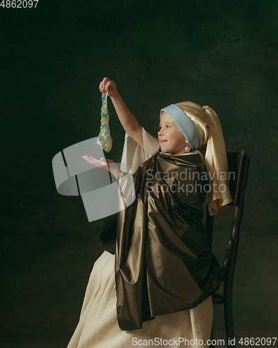 Image of Medieval little girl as a lady with a pearl earring on dark studio background. Concept of comparison of eras, childhood. Stylish creative design, art vision, new look of artwork.