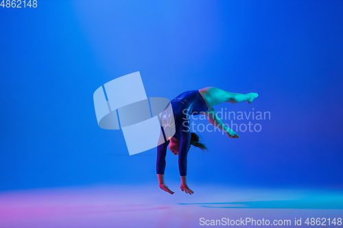 Image of Young flexible girl isolated on blue studio background. Young female model practicing artistic gymnastics. Exercises for flexibility, balance.