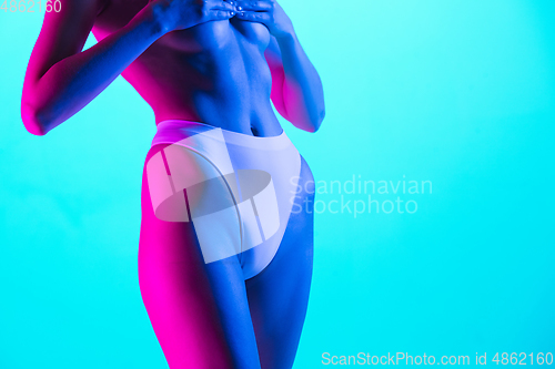 Image of Beautiful female body on blue background in purple neon light. Beauty, cosmetics, spa, depilation, diet and treatment, fitness concept.