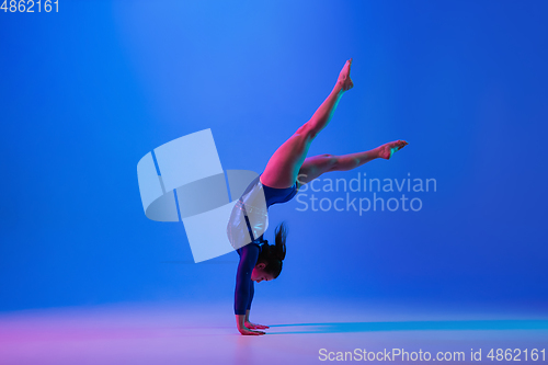 Image of Young flexible girl isolated on blue studio background. Young female model practicing artistic gymnastics. Exercises for flexibility, balance.