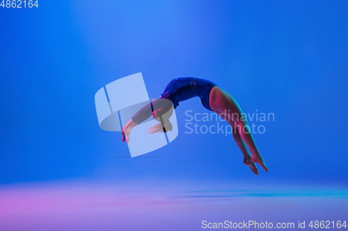 Image of Young flexible girl isolated on blue studio background. Young female model practicing artistic gymnastics. Exercises for flexibility, balance.