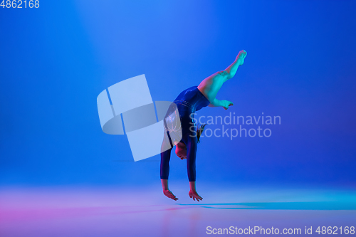 Image of Young flexible girl isolated on blue studio background. Young female model practicing artistic gymnastics. Exercises for flexibility, balance.